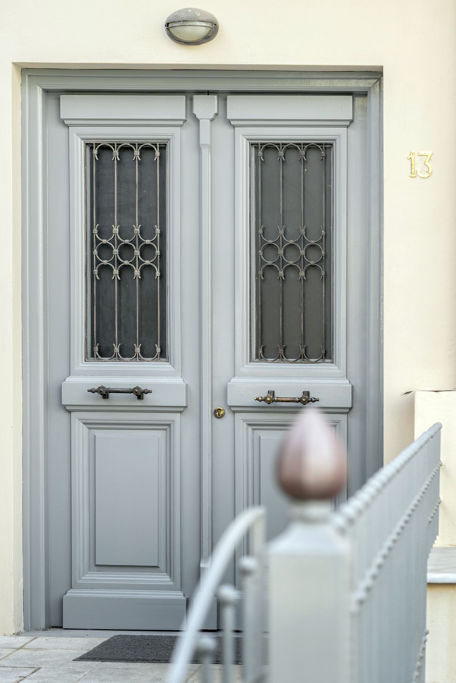 A double door with a metal grille and a brass handle, set in a light-colored wall with a number '13' above it.
