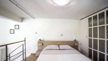 A bedroom with a wooden headboard, a bed with two pillows, a nightstand, and a wardrobe with frosted glass doors.