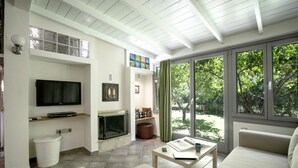 Een moderne woonkamer met een flatscreen televisie, open haard en grote ramen met uitzicht op groen.
