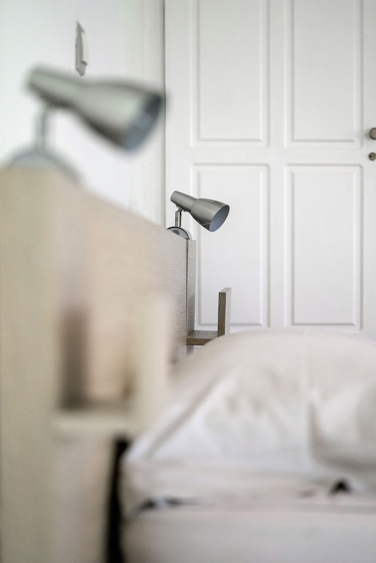 A bedroom with a bed, a bedside lamp, and a white door in the background.