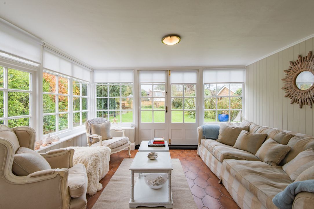 A sunroom with large windows, a white ceiling, and a cozy seating area with a sofa and armchairs.