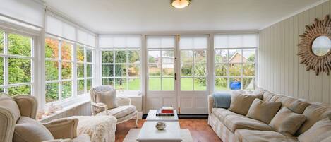 A sunroom with large windows, a white ceiling, and a cozy seating area with a sofa and armchairs.
