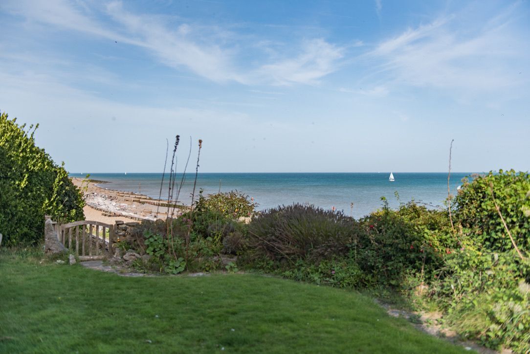 Blick auf die Küste mit einem Sandstrand, einem kleinen Segelboot und einem klaren Himmel.