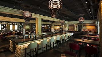 Zona de bar con barra central, diversas opciones de asientos y lámparas colgantes.