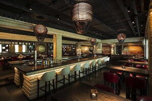 A bar area with a central bar, multiple seating arrangements, and hanging pendant lights. - Hotel Astoria (Lucerne)