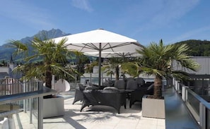 A rooftop terrace with outdoor seating, a large umbrella, and palm trees. - Hotel Astoria (Lucerne)