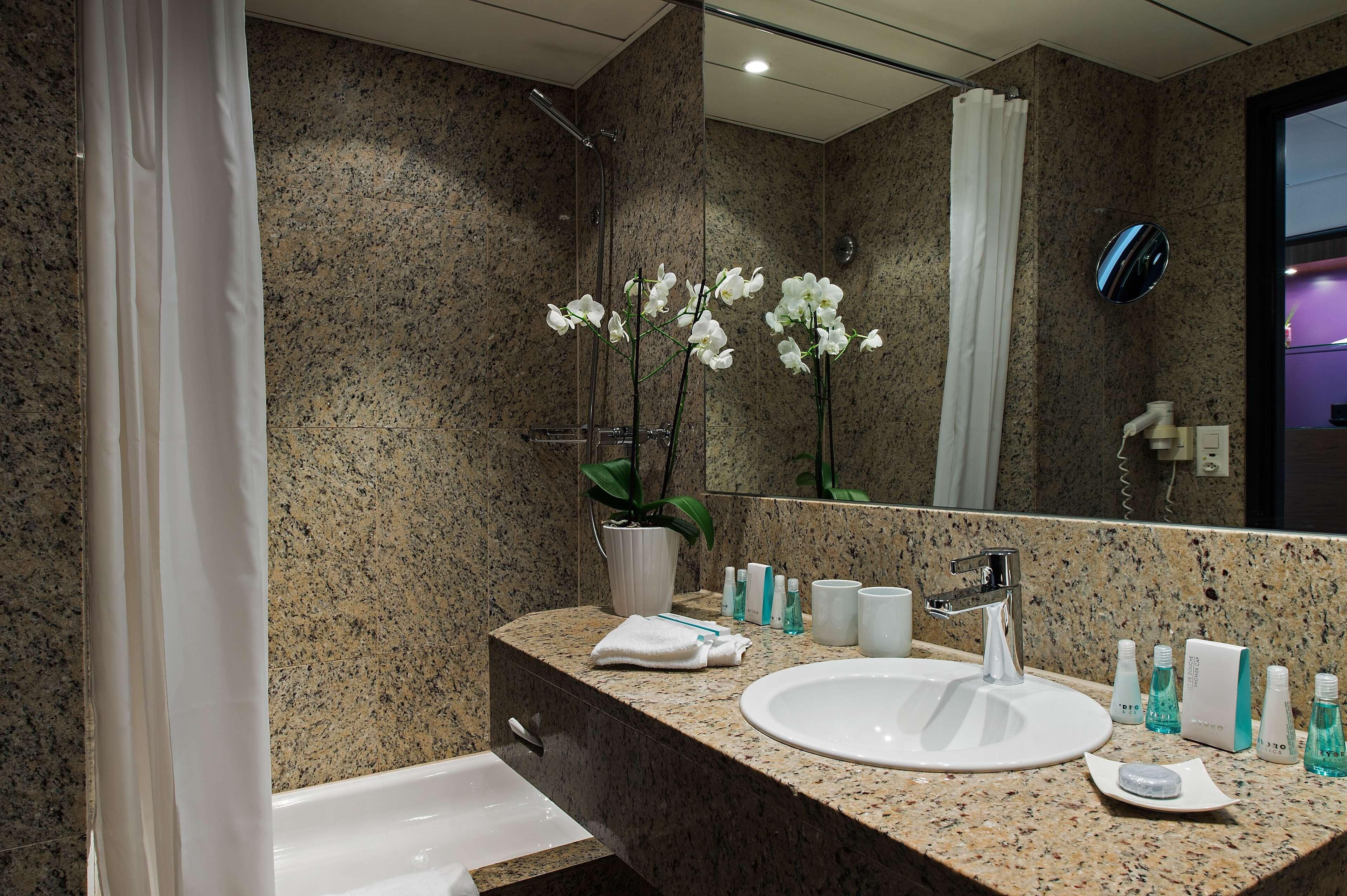 A modern bathroom with a granite countertop, white sink, and a shower area.