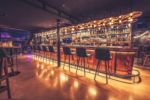 A bar area with multiple stools, a bar counter, and shelves stocked with bottles. - Hotel Astoria (Lucerne)