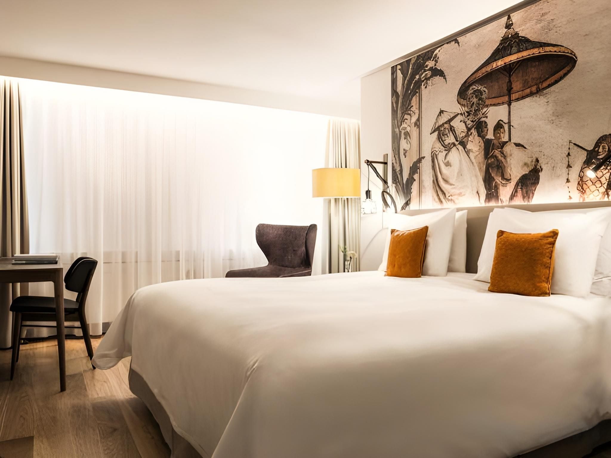 Une chambre d’hôtel avec un grand lit, un bureau, une chaise et une lampe fixée au mur.