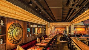 A restaurant with long communal tables, cushioned booths, and a large decorative wall.
