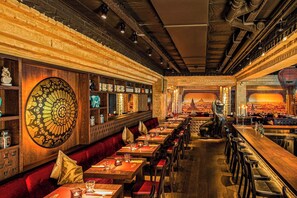 Een restaurant met lange gedeelde tafels, comfortabele zitbanken en een grote decoratieve muur.
