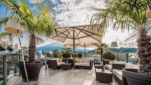 A rooftop terrace with outdoor furniture, potted plants, and umbrellas. - Hotel Astoria (Lucerne)