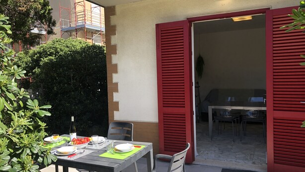 An outdoor dining area with a table set for two, red shutters, and a view of the interior. - 250 meters from the sea, air conditioning and garden, pets welcome (Cecina)