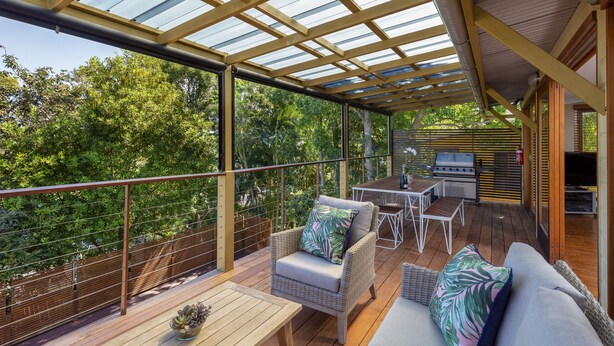 An outdoor deck with a covered area, wicker furniture, a grill, and a view of the surrounding greenery.
