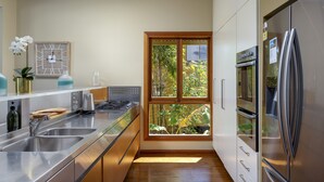 A modern kitchen with stainless steel appliances, a double sink, and a large window offering a view of greenery.