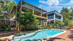 A two-story house with a swimming pool surrounded by a wooden deck.