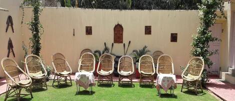 A patio with wicker chairs and a small table, surrounded by a low wall and greenery.
