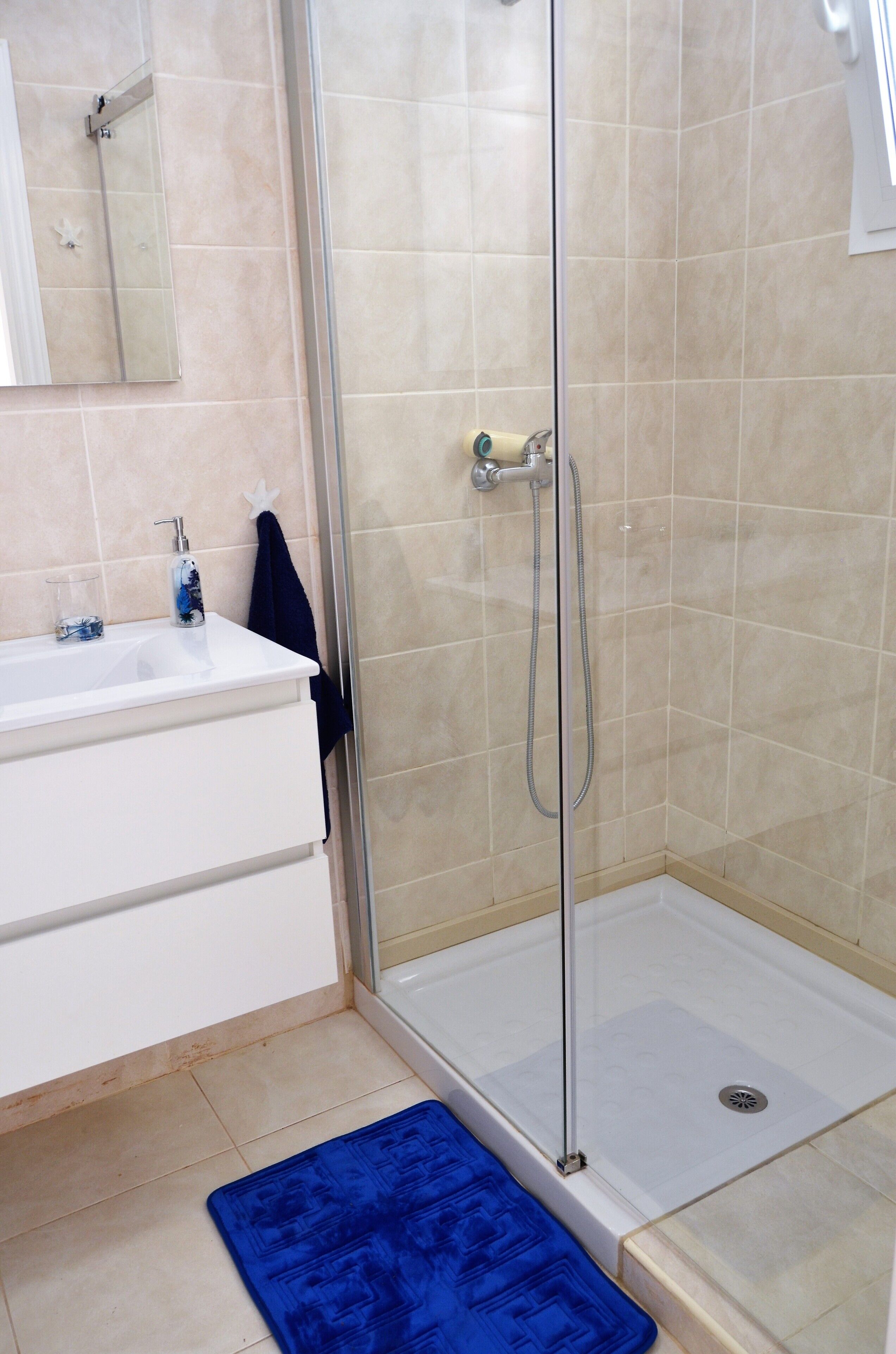 A bathroom with a glass shower enclosure, a white sink, and a blue bath mat.