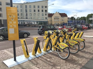 A bike station with a map and instructions, surrounded by parked cars and a building in the background. - Roost Munkkisaari (Helsinki)