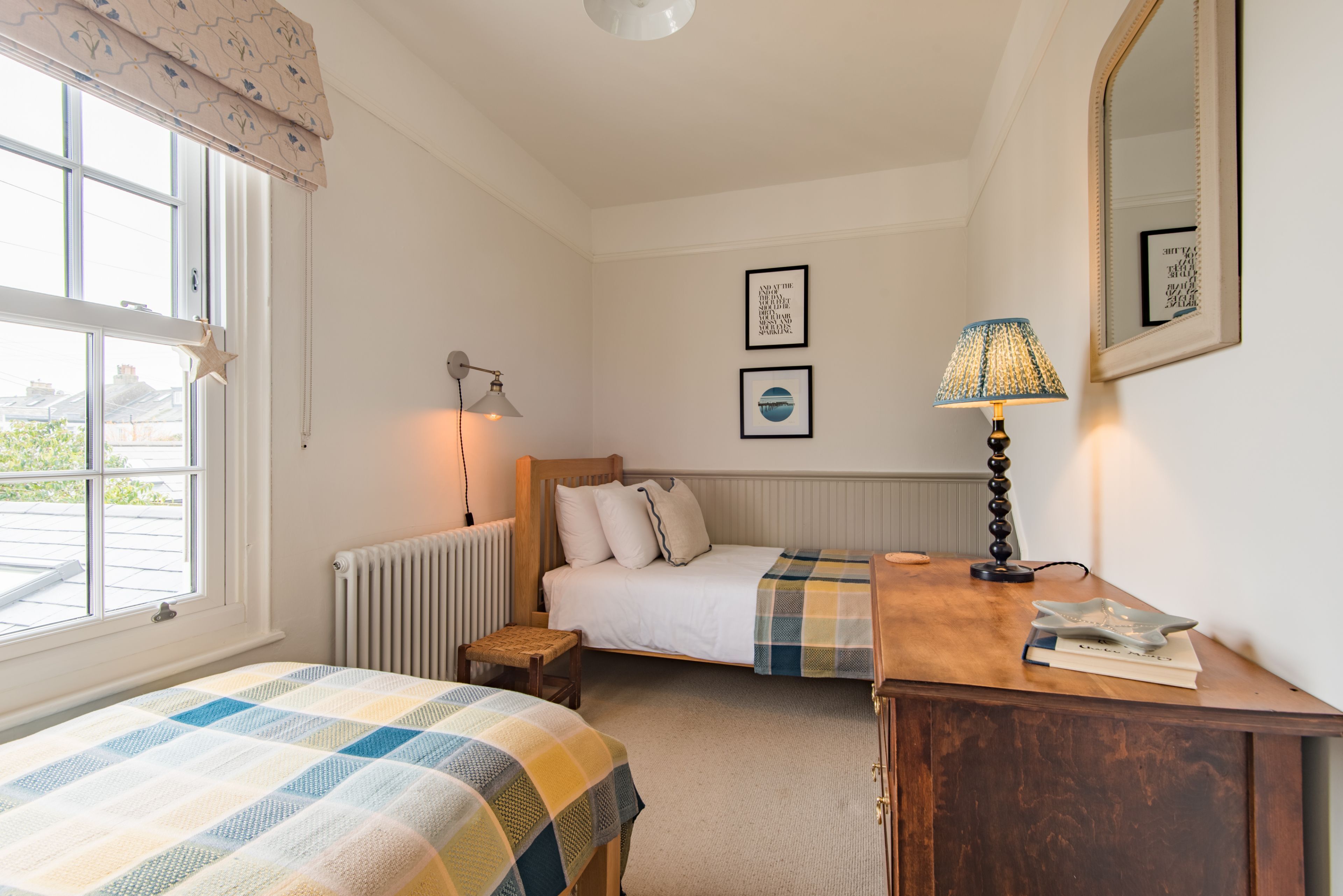 A bedroom with two beds, a wooden dresser, a lamp, and a window with a star decoration.