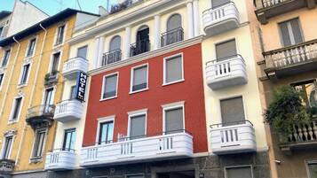 Un edificio a più piani con facciata rossa, balconi e una insegna che indica che si tratta di un albergo.