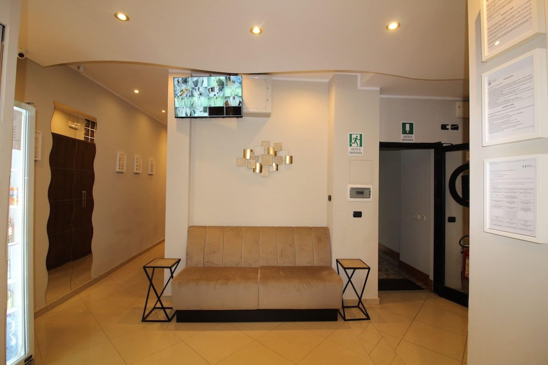Un vestíbulo con un sofá, un televisor montado en la pared y una puerta con letrero de salida de emergencia.