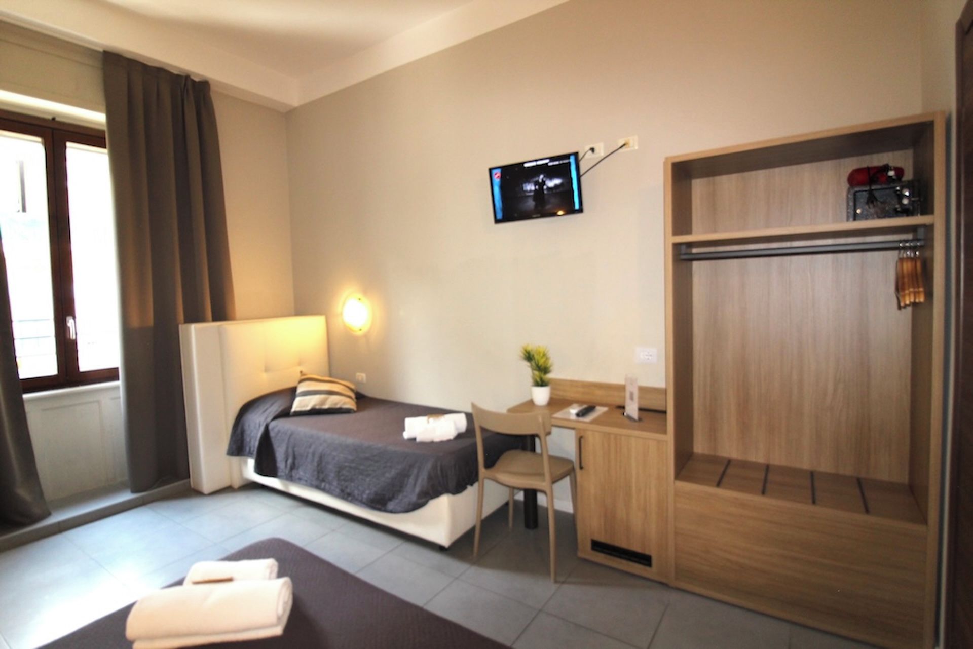 A hotel room with a bed, a desk, a chair, a television, and a wardrobe.