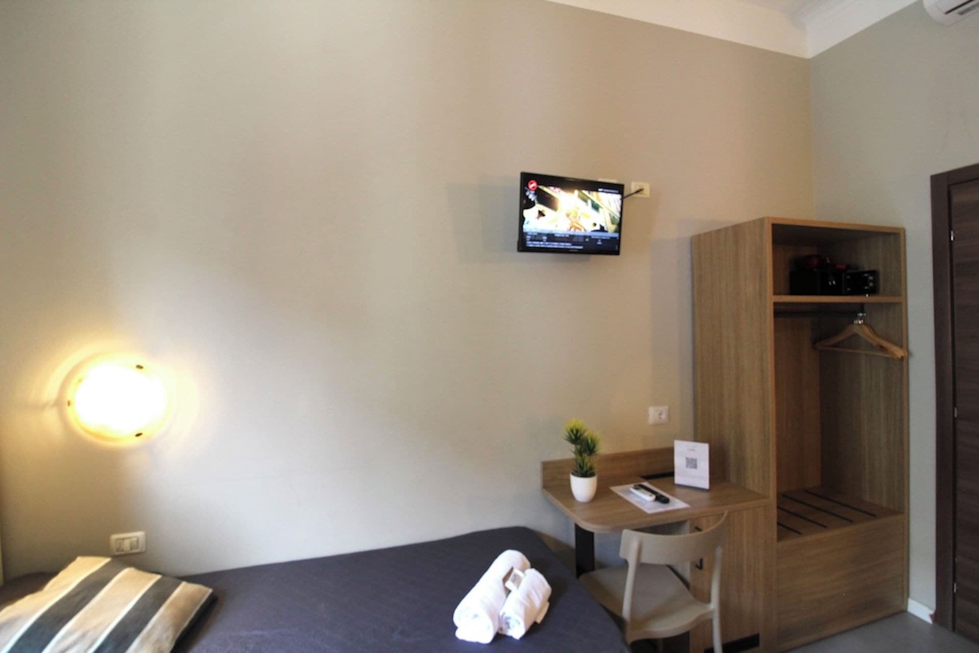 Une chambre d’hôtel comprenant un lit, un bureau avec une chaise, un téléviseur fixé au mur et une armoire.