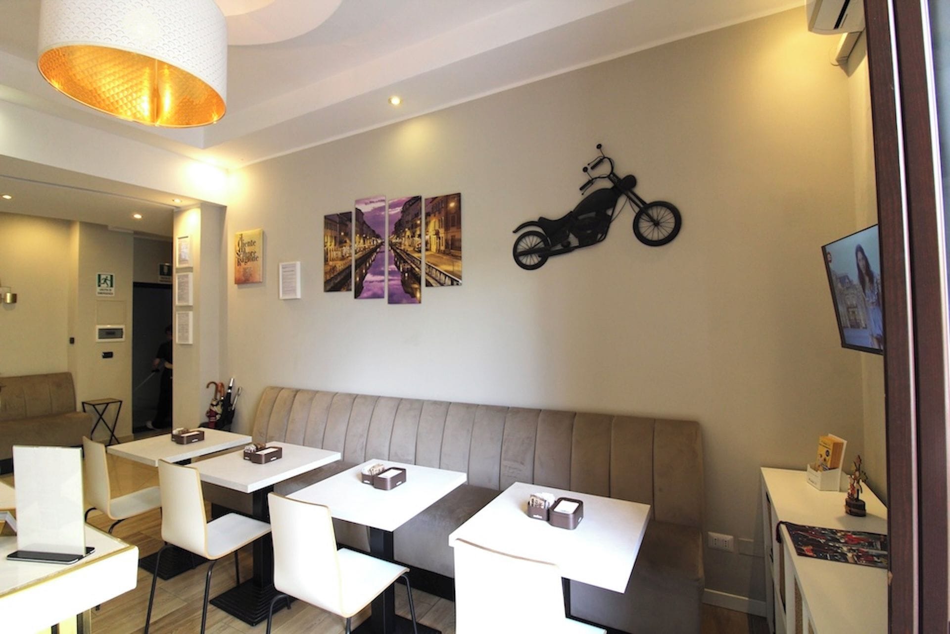 Un espace repas moderne avec des banquettes et des tables, une décoration murale sur le thème de la moto et un luminaire suspendu au plafond.