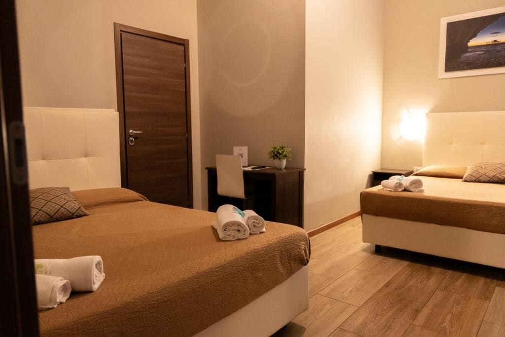 Een hotelkamer met twee bedden, een houten deur, een tafeltje met een plant en een lampje aan de muur.