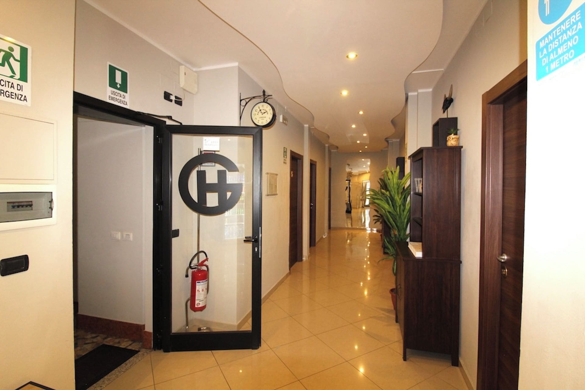 Un couloir d’hôtel avec un extincteur fixé au mur, une horloge et un panneau indiquant la distance jusqu’à la station de métro.