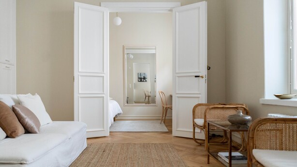 A modern, minimalist bedroom with a white bed, a white sofa, and a wicker chair. - Roost Roobert (Helsinki)