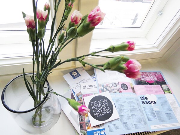 A window with a view of a building, a vase with pink flowers, and a table with brochures and a map.