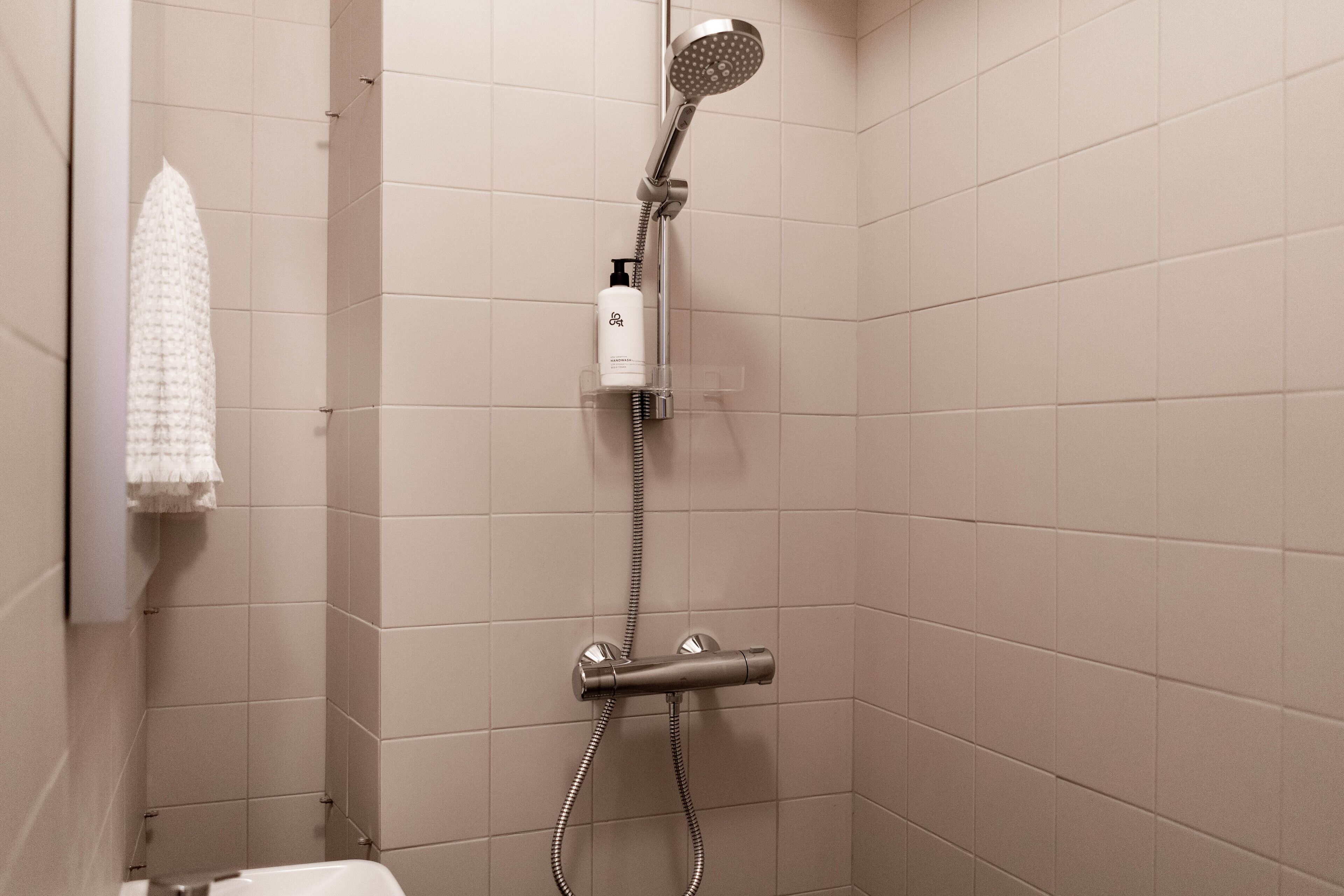 A shower with a handheld showerhead, a handheld shower attachment, and a bottle of shampoo.