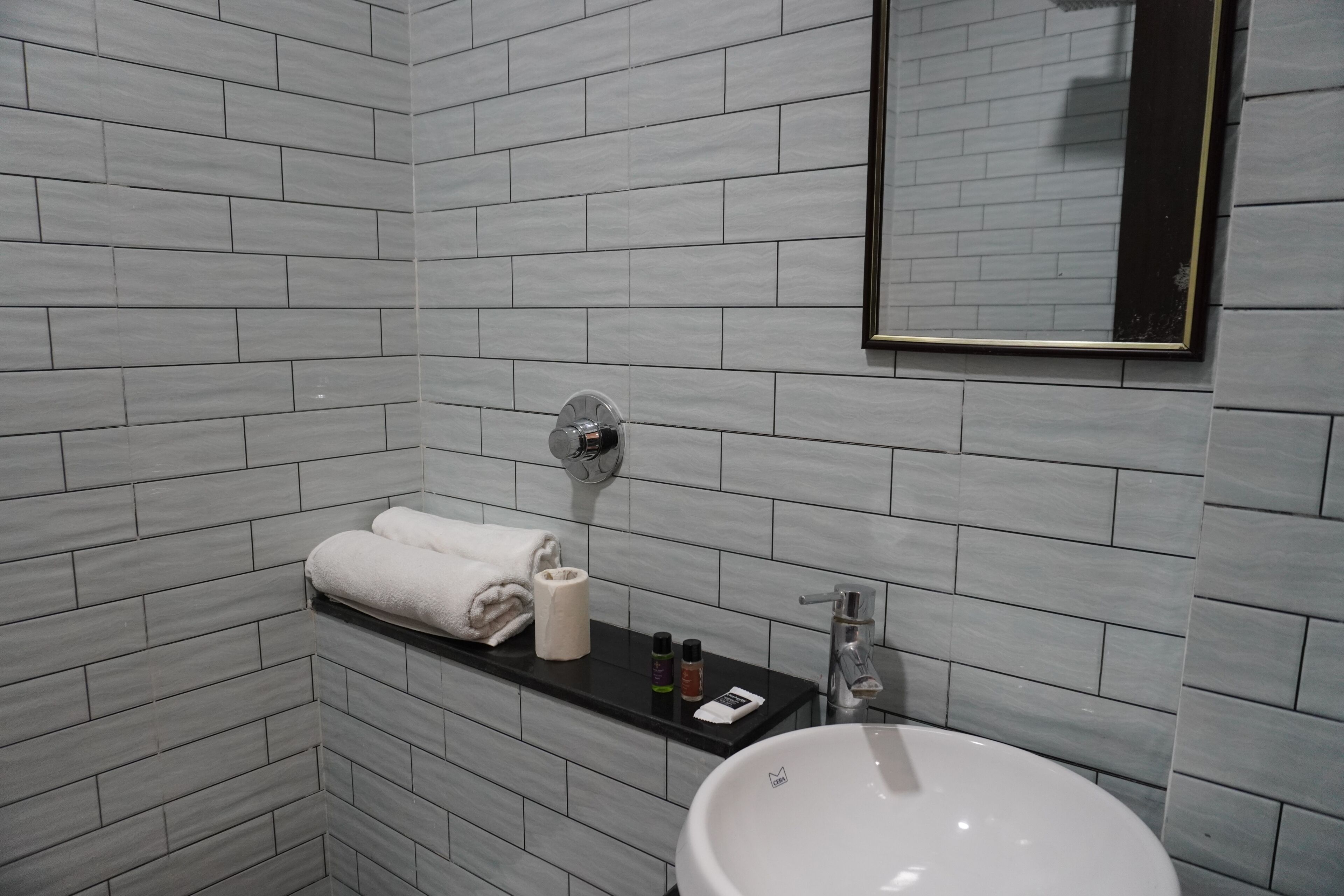 A bathroom with grey tiled walls, a white sink, a towel rack, and a mirror.