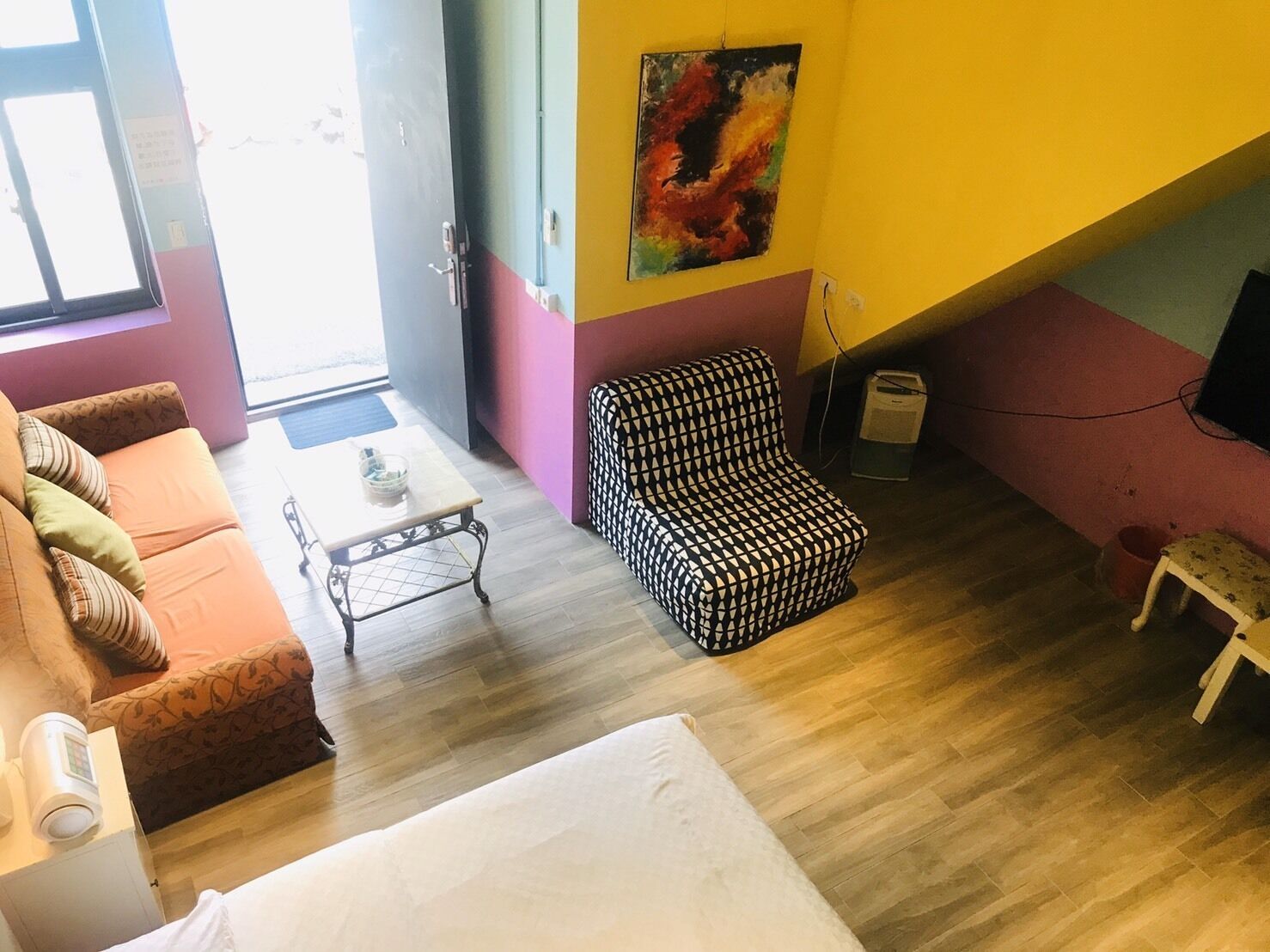 A room with a sofa, a patterned armchair, a small table, and a bed.