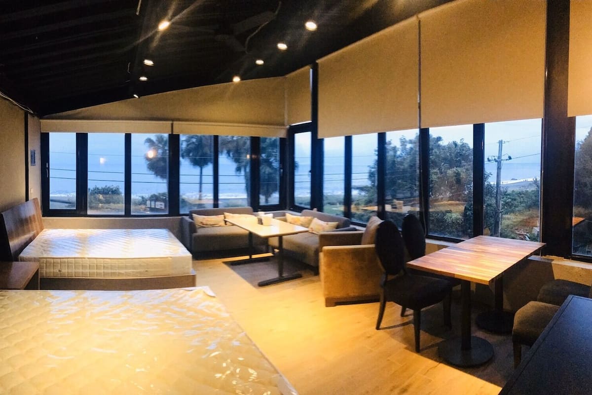 A modern hotel room with a large bed, a sofa, a dining table, and a view of the ocean.