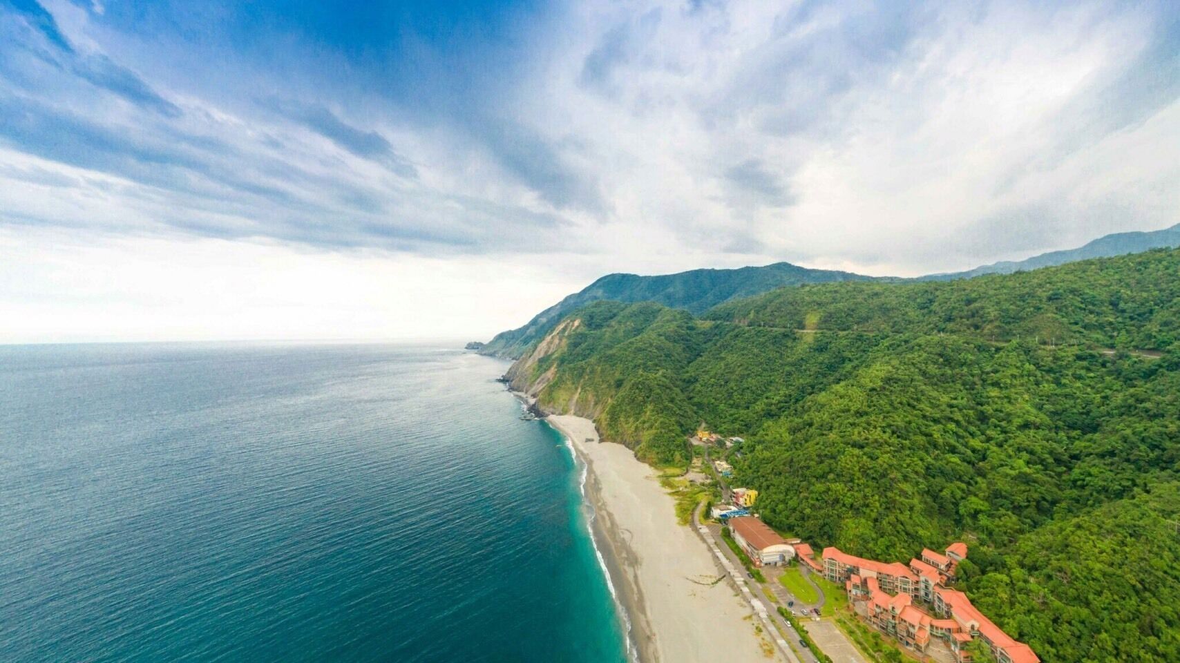 A coastal landscape with a beach, a road, and buildings with red roofs.