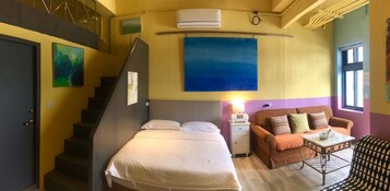 Una habitación con una cama, un sofá, una mesita, una lámpara y un cuadro en la pared.