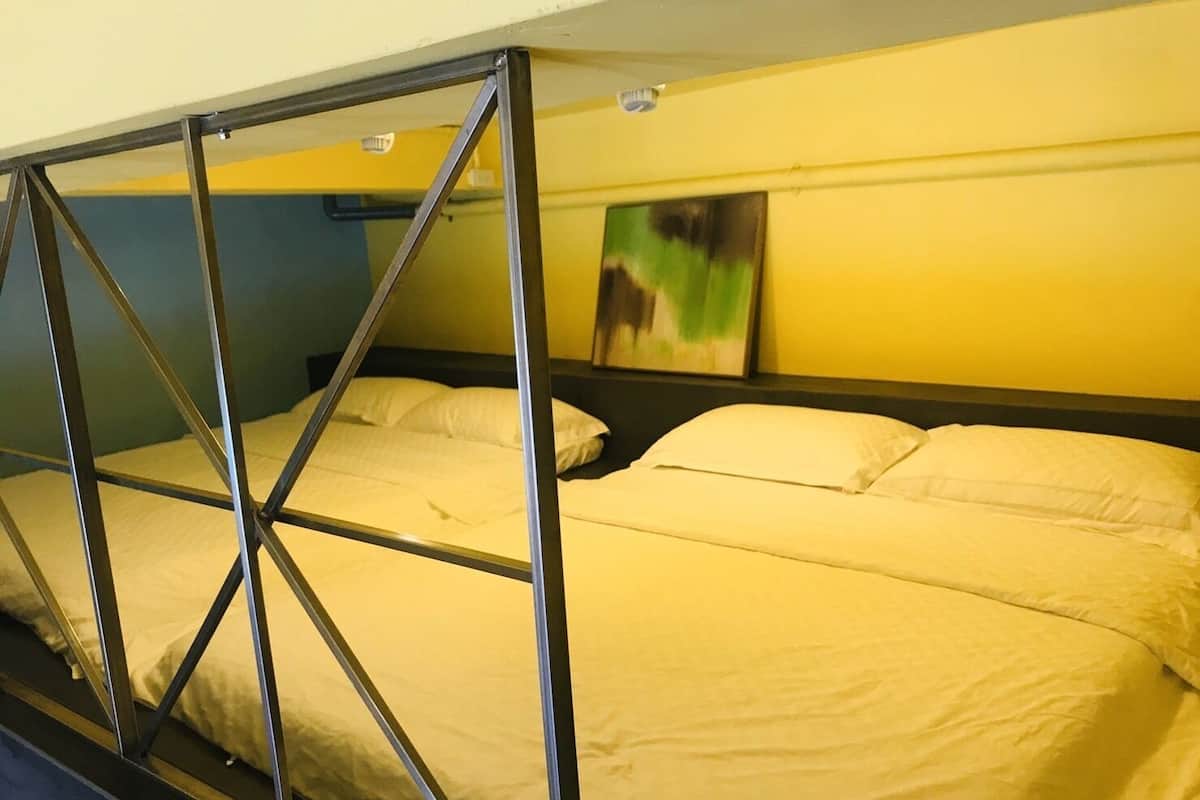 A bunk bed with metal frames and white bedding in a room with yellow walls and a painting on the wall.