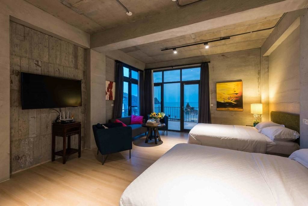 A hotel room with two beds, a flat-screen TV, a sofa, a small table with a vase, and a painting on the wall.