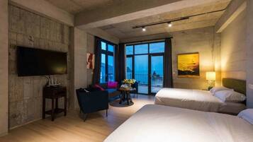 A hotel room with two beds, a flat-screen TV, a sofa, a small table with a vase, and a painting on the wall.