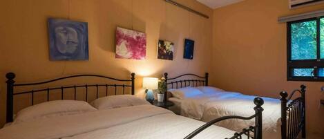 A bedroom with two beds, a nightstand with a lamp, and wall art.