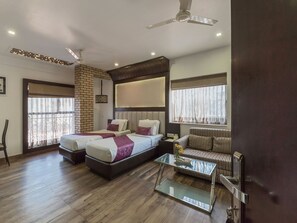 A hotel room with two beds, a sofa, a glass coffee table, and a ceiling fan. - Treebo Tryst Ivory (Kolkata)