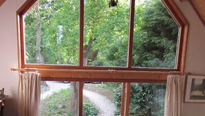 Ein Zimmer mit großem Fenster, Korbsessel, Holztisch und einem Bett.