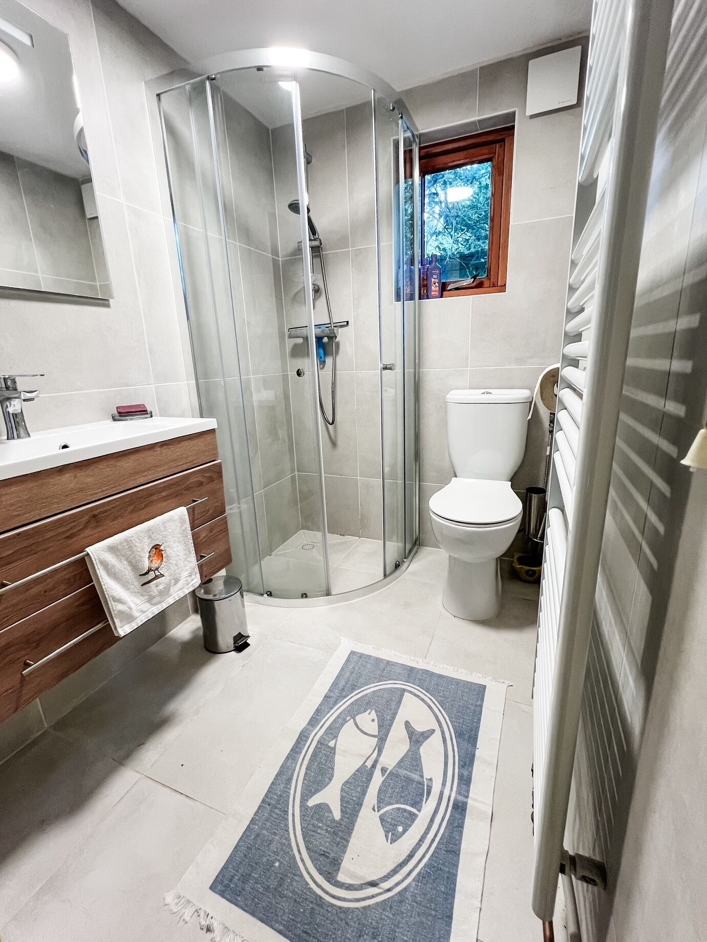 Une salle de bain moderne avec une douche à parois de verre, des toilettes et un meuble-lavabo sur lequel est accrochée une serviette.