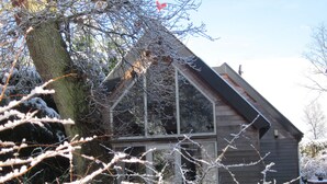 Eine Holzhütte mit geneigtem Dach und großen Fenstern, umgeben von mit Schnee bedeckten Ästen.