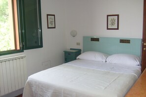 A bedroom with a bed, a nightstand, a window, and two wall-mounted pictures.