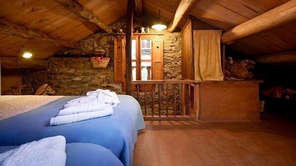 Une chambre confortable située dans les combles, avec un mur en pierre, des poutres apparentes, un balcon et un lit avec une literie bleue.
