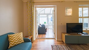 A living room with a sofa, a television on a cabinet, and a patterned curtain. - Modern holiday home in Walmer, Deal with parking (Deal)